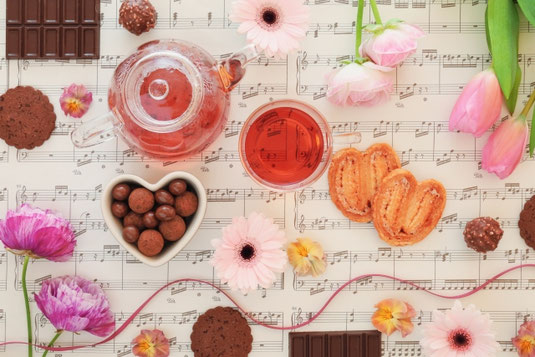 楽譜の上に置かれたティーセット。チョコレート、クッキー、パイ。チューリップとガーベラの花。習い事。