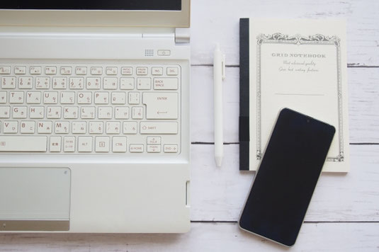 木目調のデスクに広げられたリングノートとボールペン。小皿に盛られたハート形のココアクッキー。コーヒーの入ったマグカップ。