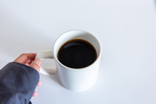 コーヒーの入ったマグカップを手に取るシャツ姿の女性。