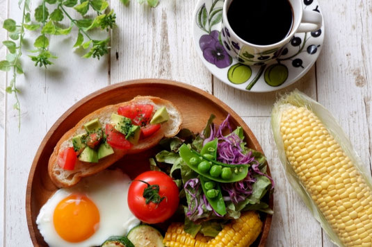 お皿に並べられた輪切りの野菜とフルーツ。水の入ったグラスとナイフ&フォーク。健康的な食事。