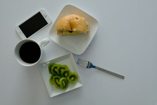 朝の食卓。ベーグルのサンドイッチ。スライスされたキウイフルーツ。コーヒー。傍らにスマートフォン。代休。