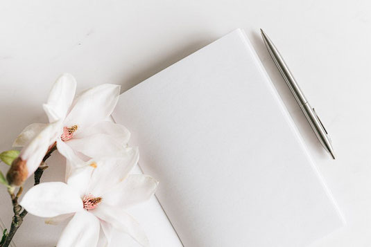 オフィスのデスクに積まれた書籍。黄色の水仙が活けられたガラスの花びん。