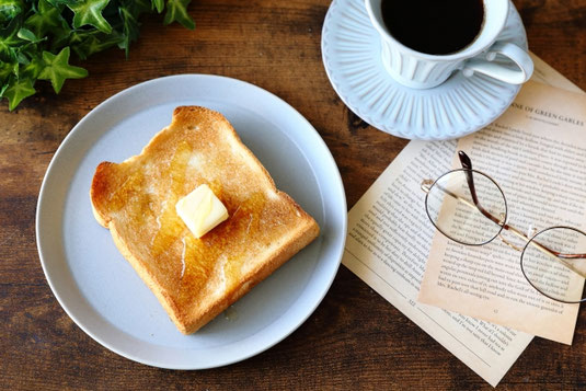 バタートーストのお皿。コーヒーの入ったカップ＆ソーサ。資料ペーパーのうえに置かれた眼鏡。出勤前のテーブル。