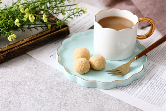 タブロイド紙の上に置かれたクッキーのお皿とカフェオレのマグカップ。フォトフレームのうえに無造作に置かれたグリーン。