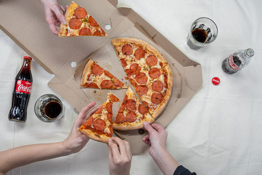 デリバリーピザをシェア。めいめいピザに手を伸ばす。瓶のコカ・コーラがグラスに注がれている。