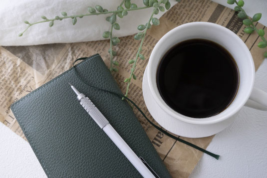 手帳の上にシャープペンシルが置かれている。コーヒーの入った白のカップ。