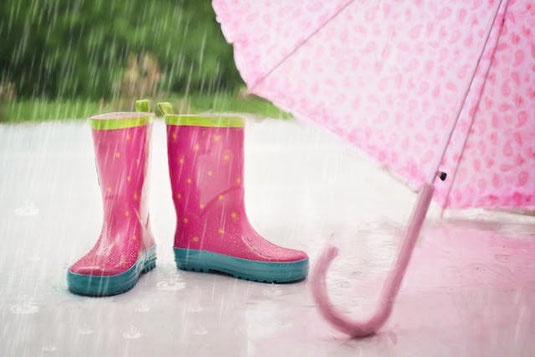 雨に濡れるピンク色のレインブーツと雨傘。