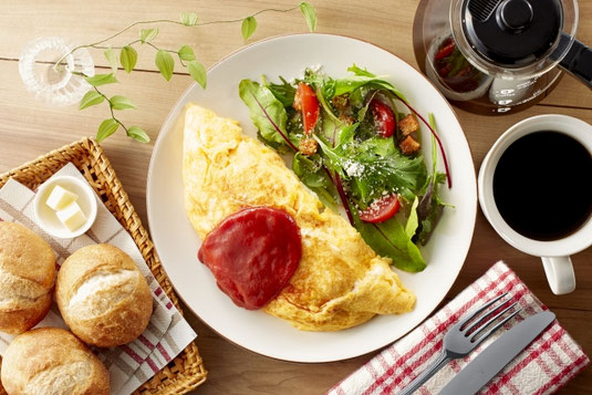 オムレツとサラダのプレート。フランスパンとバターが盛り付けられた籠。コーヒーのマグカップとサーバー。健康的な食事。