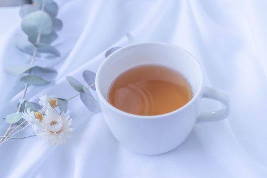 ベッドリネンのうえに置かれた紅茶のカップ。ユーカリの小枝と白色の花。