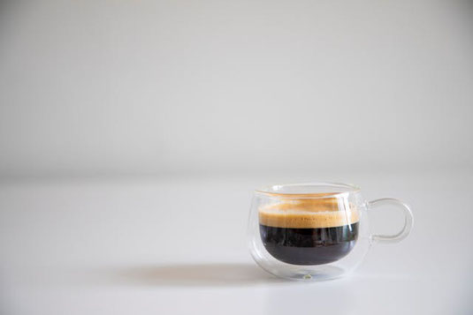 打ち合わせのためカフェに赴くビジネスマン。チノパンと紺のジャケット。手にした手帳とコーヒー。