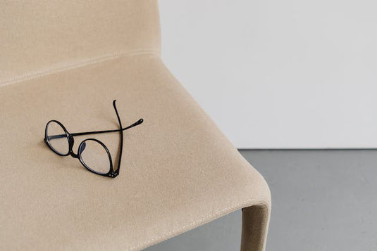 ソファタイプの椅子の上に置かれた黒縁眼鏡。