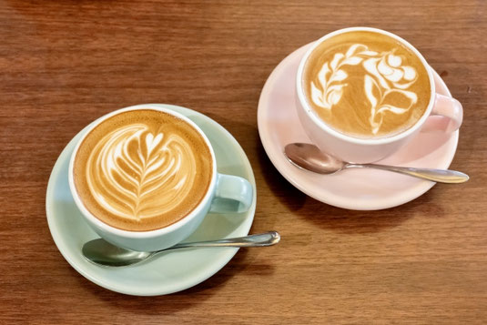 ラテアートが描かれたカフェラテのカップ＆ソーサが2客並んでいる。水色とピンク色のカップ＆ソーサ。