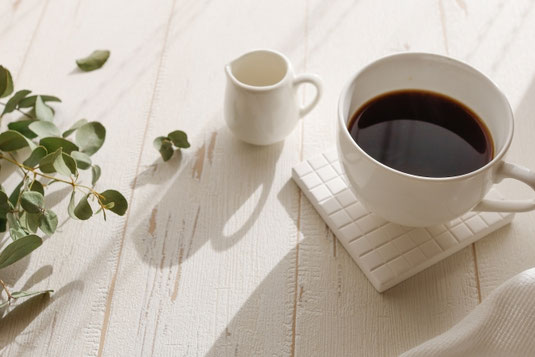 コーヒーの入ったカップとミルクピッチャー。ユーカリの小枝。