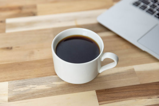 ノートパソコンの前に置かれたコーヒーのマグカップ。