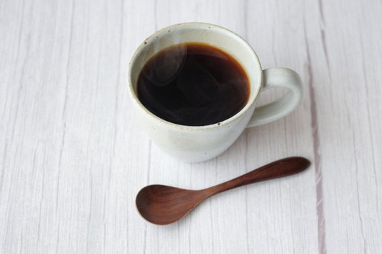 コーヒーの入ったマグカップと木製のコーヒースプーン。