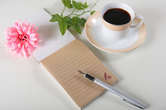メモ帳と万年筆。ダリアの花。コーヒーの入ったカップ&ソーサ。