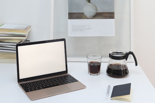 ノートパソコン。広げられたハードカバーの洋書。コーヒーの入ったカップ&ソーサ。観葉植物のグリーン。
