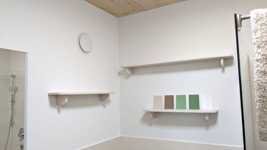 Drei in "Soft Beige" lackierte Badregale an der Wand, auf dem niedrigsten stehen fünf Farbkarten in Grün und Brauntönen. Links oben ist ein runder weißer Lüftungsauslass zu sehen.