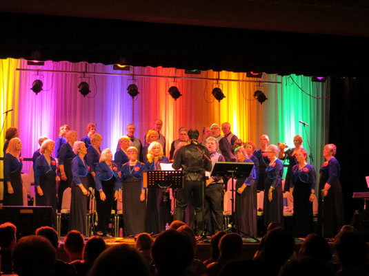 Wessex Chorus choir singing on the Barrington Theatre stage with rainbow coloured lighting.