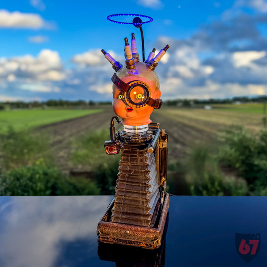 Strampelchen is an assemblage artwork made of historic parts: doll head, spark plugs, plate camera. Illuminated by LEDs and animated with an integrated motor.