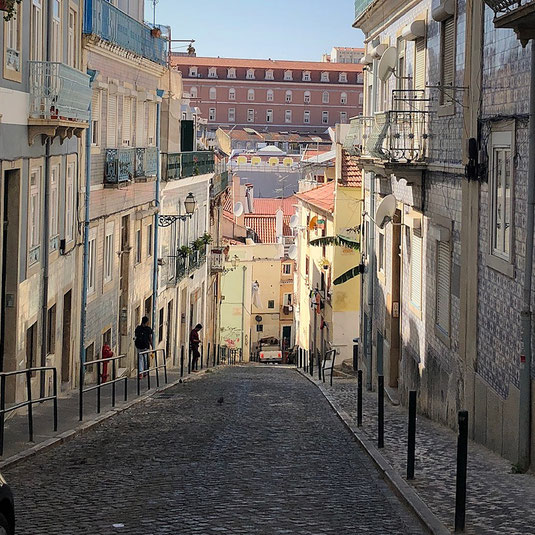 Strasse Gasse in Lissabon im Stadtteil Mouraria steil hinauf mit Kopfsteinpflaster und Tuktuk 