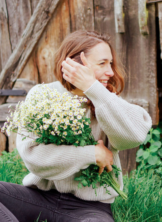 Junge Frau sitzt mit einem Blumenstrauß vor einer Scheune