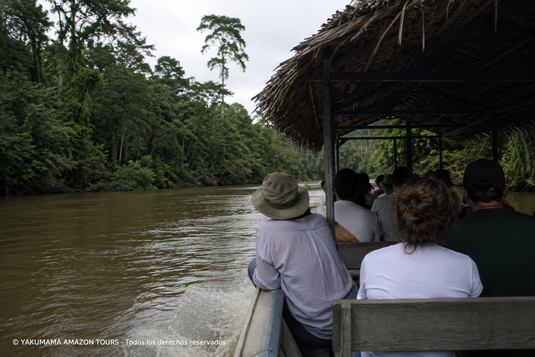 Turistas navegando en un bote tradicional por un río amazónico cerca de Iquitos, camino hacia un albergue en la selva durante un tour por la Amazonía peruana.
