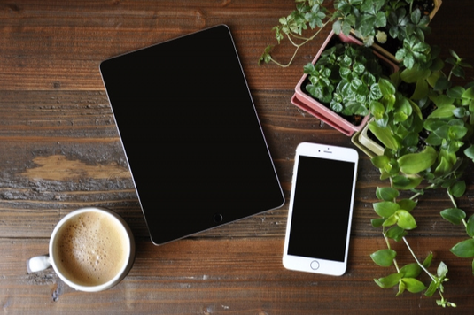 テーブルに置かれたタブレットとスマートフォン。コーヒーの入ったマグカップ。グリーンの鉢植。