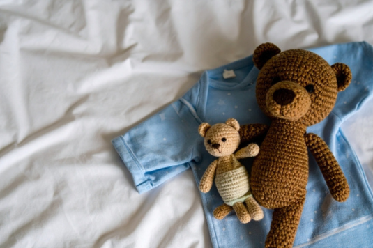 ベッドリネンの上に広げられた子供服とクマのぬいぐるみ。子育て。