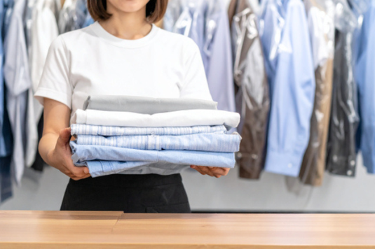クリーニング店で畳まれたシャツを両手に抱える女性。パート社員。