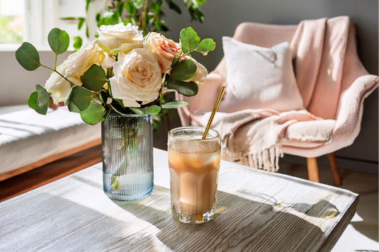 テーブルに飾られたバラの花とアイスコーヒーのグラス。一人掛けのソファとクッション。お休みの日。