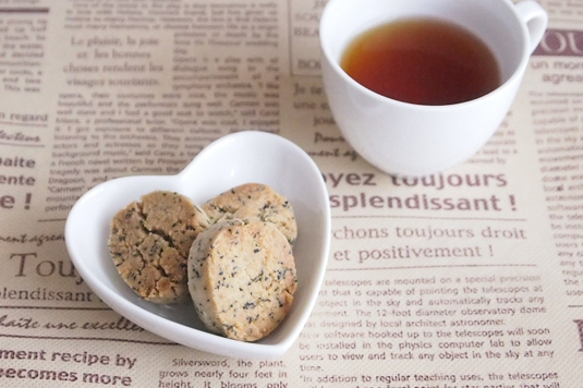 タブロイド紙の上に置かれた紅茶のカップ。ハート形のお皿に盛り付けれられた紅茶のクッキー。
