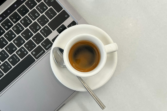ノートパソコンのキーボードのうえにコーヒーの入ったカップ&ソーサ。