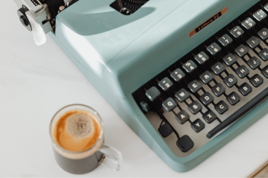 ノートパソコンと資料。資料のうえに置かれたコーヒーの入ったマグカップ。白のバラ。