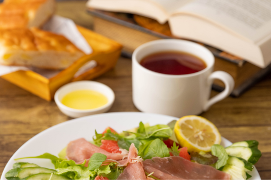 サラダとフォカッチャの朝食。紅茶の入ったマグカップ。ページがめくられた本。