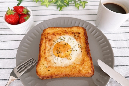 目玉焼きがのったトーストパンのお皿とナイフ&フォーク。イチゴが盛り付けられた器。コーヒーの入ったマグカップ。