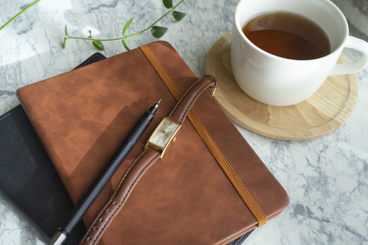 オフィスのテーブルでコーヒーを飲みながらノートパソコンを広げる男性。チェック柄のジャケット。観葉植物。