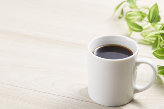 デスクにコーヒーの入ったマグカップ。グリーンの葉。