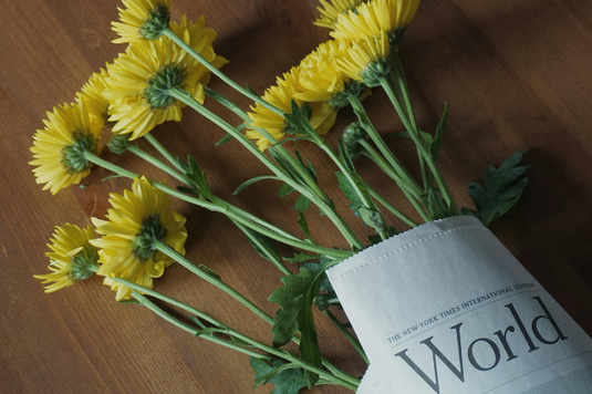 英字新聞にくるまれた黄色のスプレーマムの花たち。無造作にテーブルに置かれている。