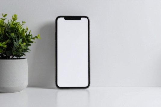 オフィスのテーブルに立てかけられたスマートフォン。隣にグリーンの鉢植が飾られている。