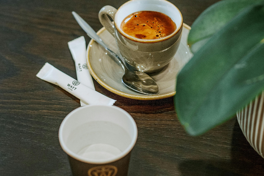 カフェのテーブルに並べられたランチメニュー。試食する店長。感想をメモするパート社員。緑のエプロン姿。
