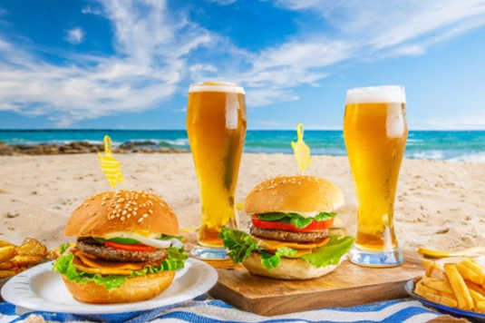 青空のビーチ。レジャーシートのうえにハンバーガーとビールのグラス。社内行事。