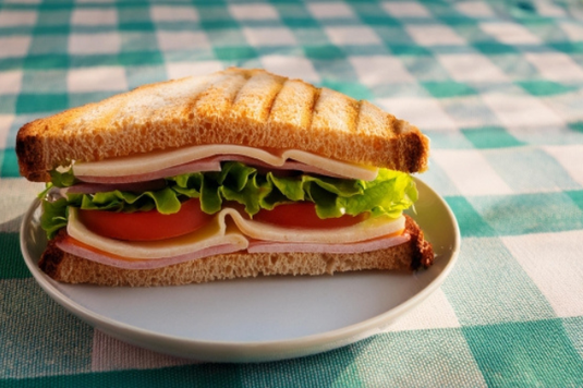 レタス、ハム、チーズ、トマトのサンドイッチ。格子模様のクロス。