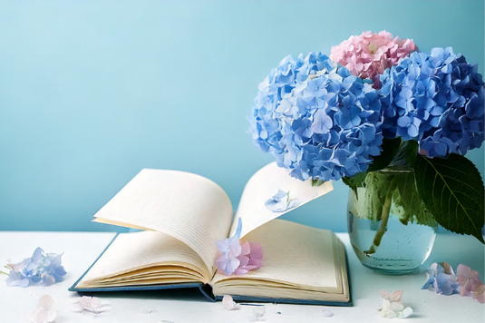 ページがめくられたノートのうえに花びらがはらり。となりにアジサイが生けられたガラスの花瓶。