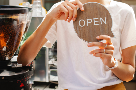 チェックのシャツと赤いエプロンの店員。売り上げをチェック表に記入する正社員と説明するパート社員。