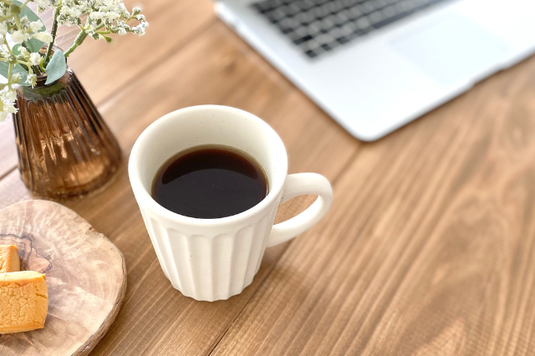 ノートパソコンの傍らにクッキーのお皿とコーヒーの入ったマグカップ。グリーンが生けられた小さなガラスの一輪挿し。
