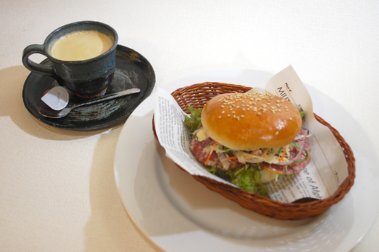 英字新聞が敷かれた籐のトレイにのったハンバーガー。コーヒーの入ったカップ&ソーサ。