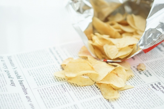 袋のパッケージを開封し、英字新聞のうえに広げられたポテトチップス。
