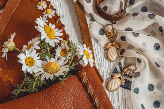 革のショルダーバッグに詰められたカモミールの花。イヤリングと水玉模様のスカーフ。