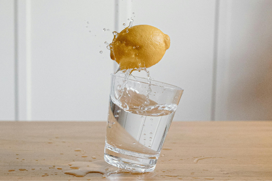水の入ったグラスに投げつけられたレモン。グラスが傾いて水がこぼれている。